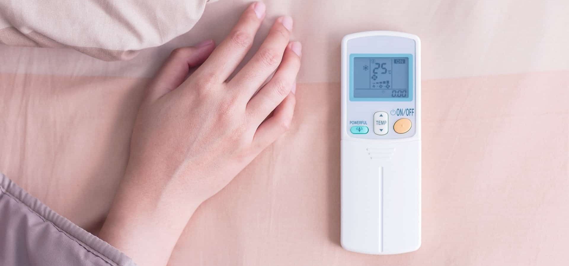 Woman hand under blanket with remote control air-conditioner.
