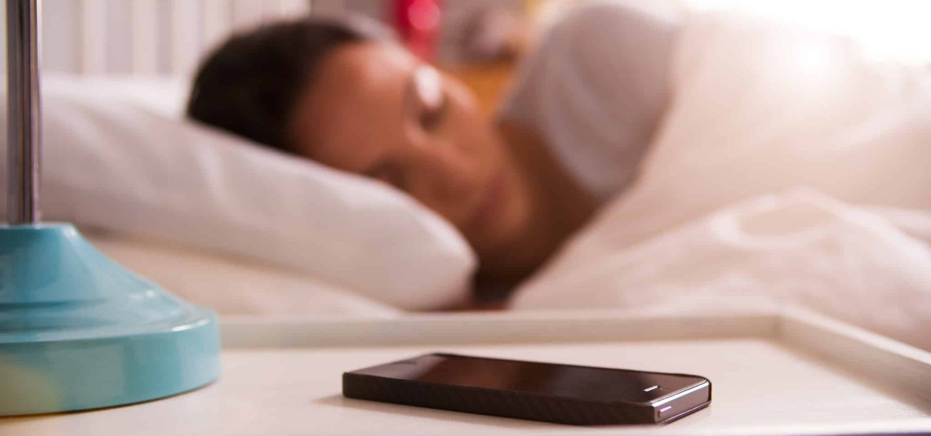 Woman Asleep In Bed Using Alarm On Mobile Phone