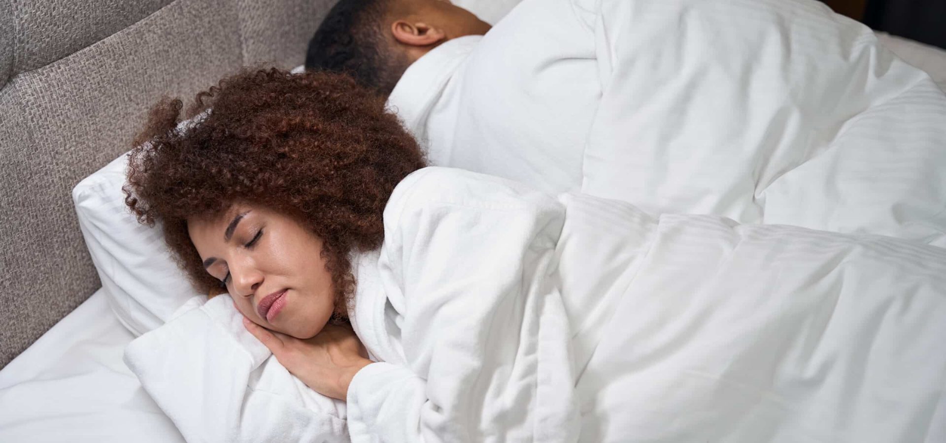 Guy and his girlfriend sleep in hotel room, turned away from each other, the guys are located on large bed